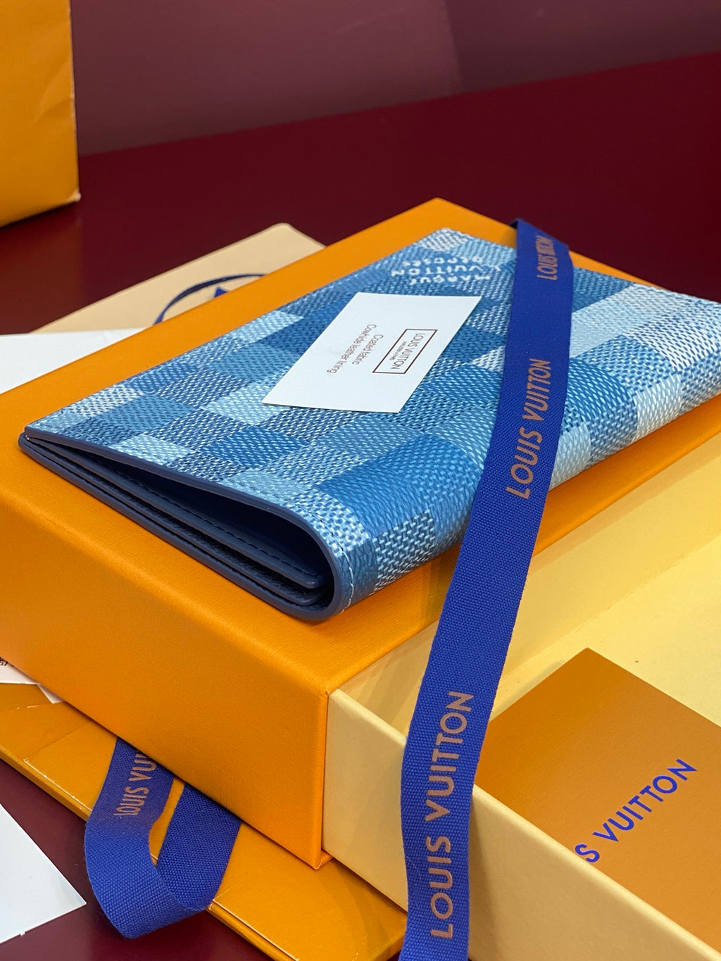 Louis Vuitton blue checkered canvas wallet-style bag on box with blue ribbon