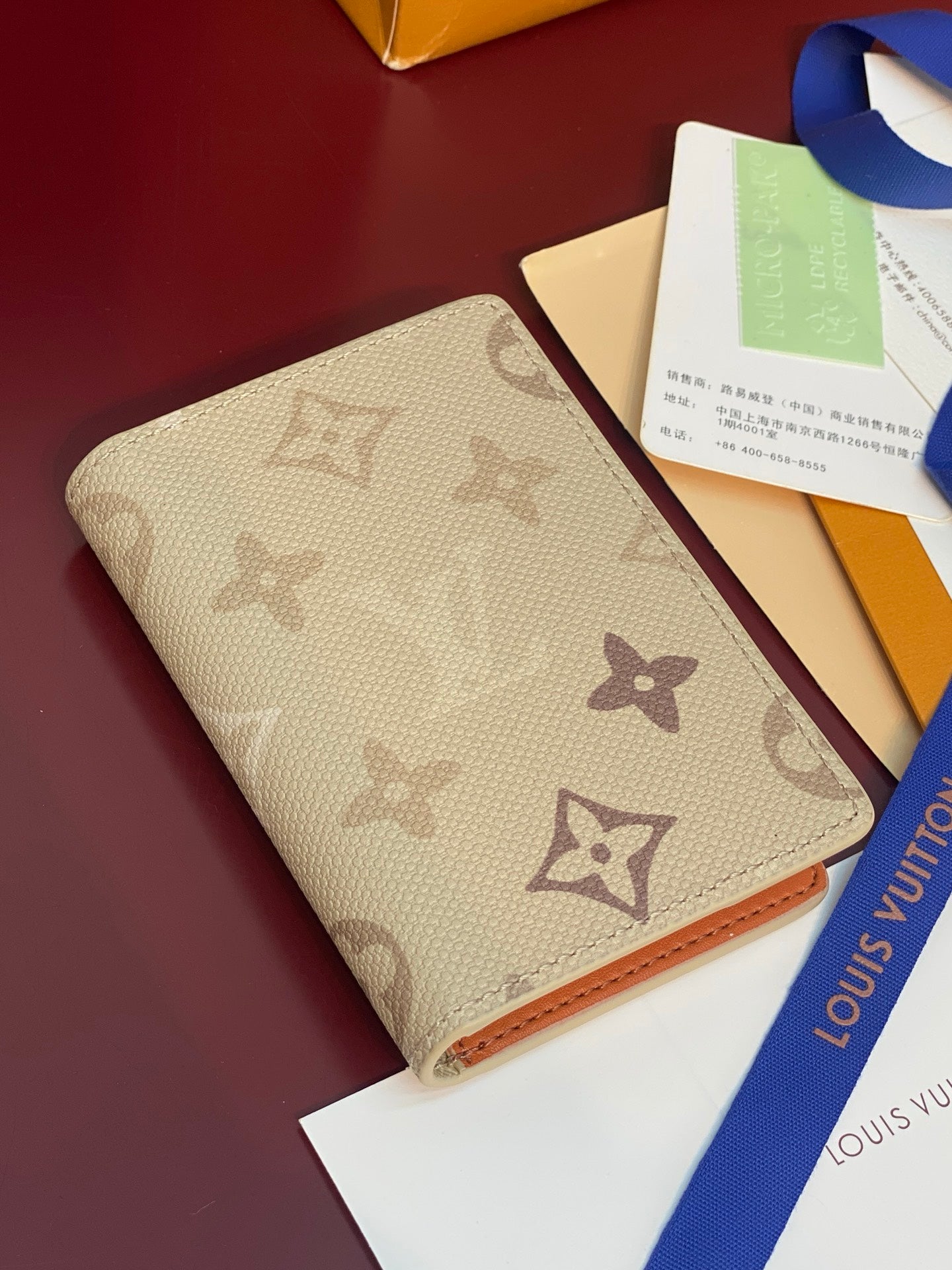Monogram card holder, beige canvas exterior with brown icons and orange trim at edges