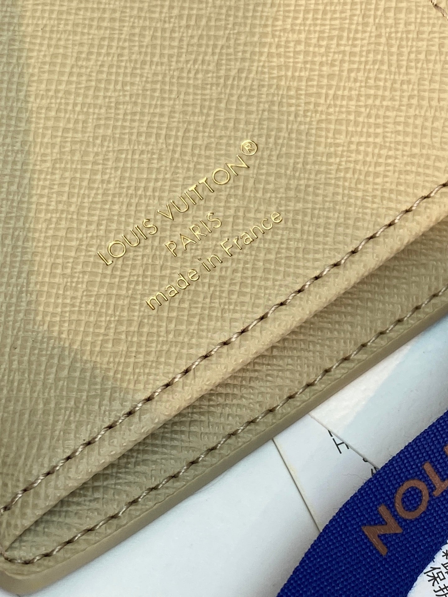 Beige monogram wallet close-up showing stitched edge and embossed brand text.