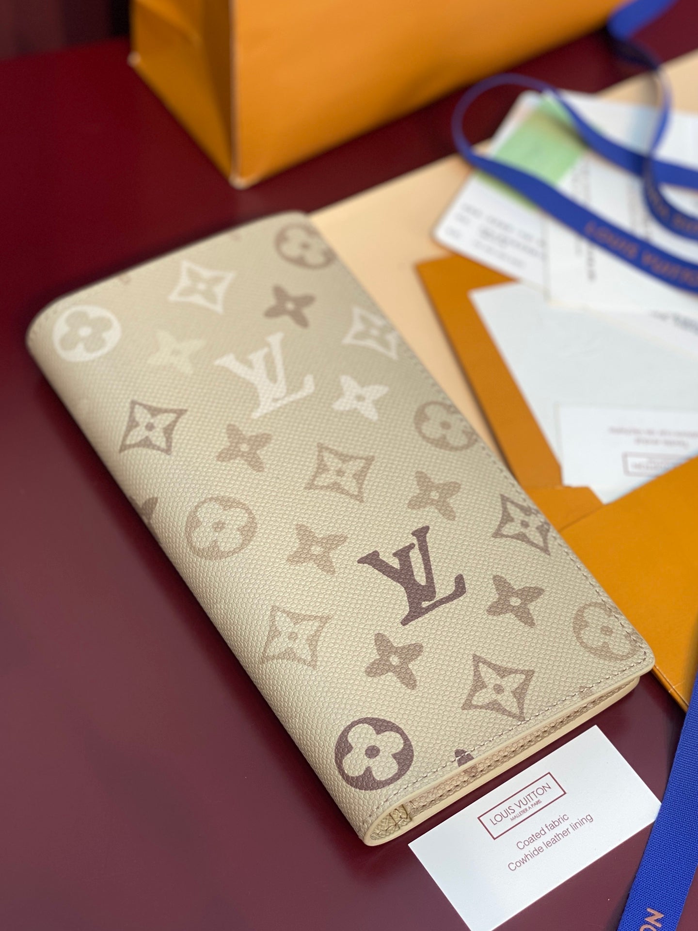 Beige monogram canvas wallet with gold-toned trim and flat front pocket.
