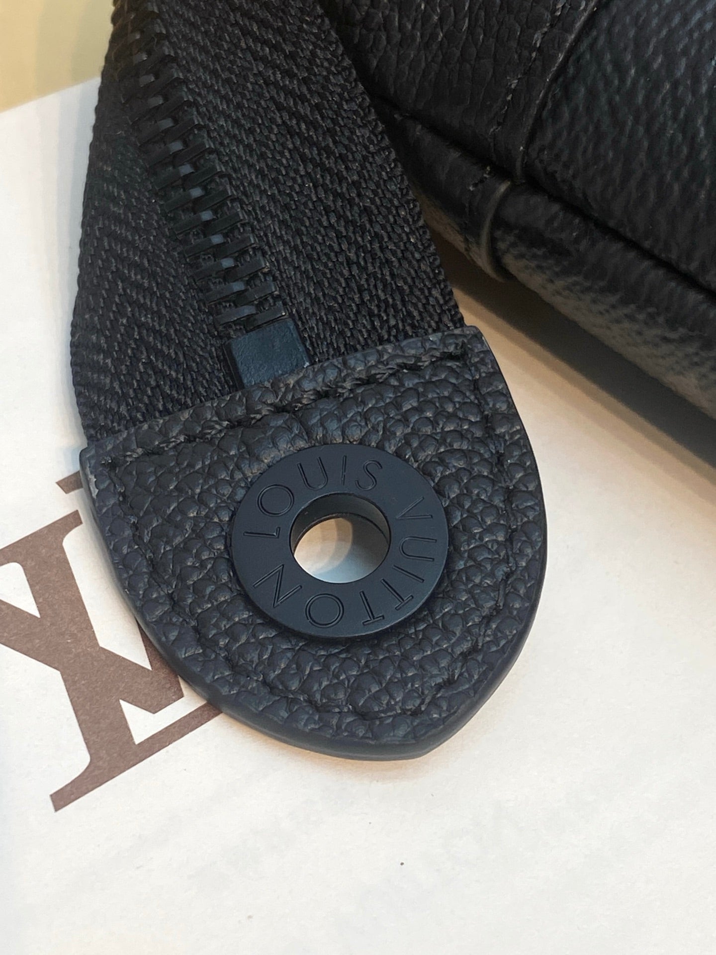 Louis Vuitton leather clutch bag close-up of wrist strap ring on dark textured leather.