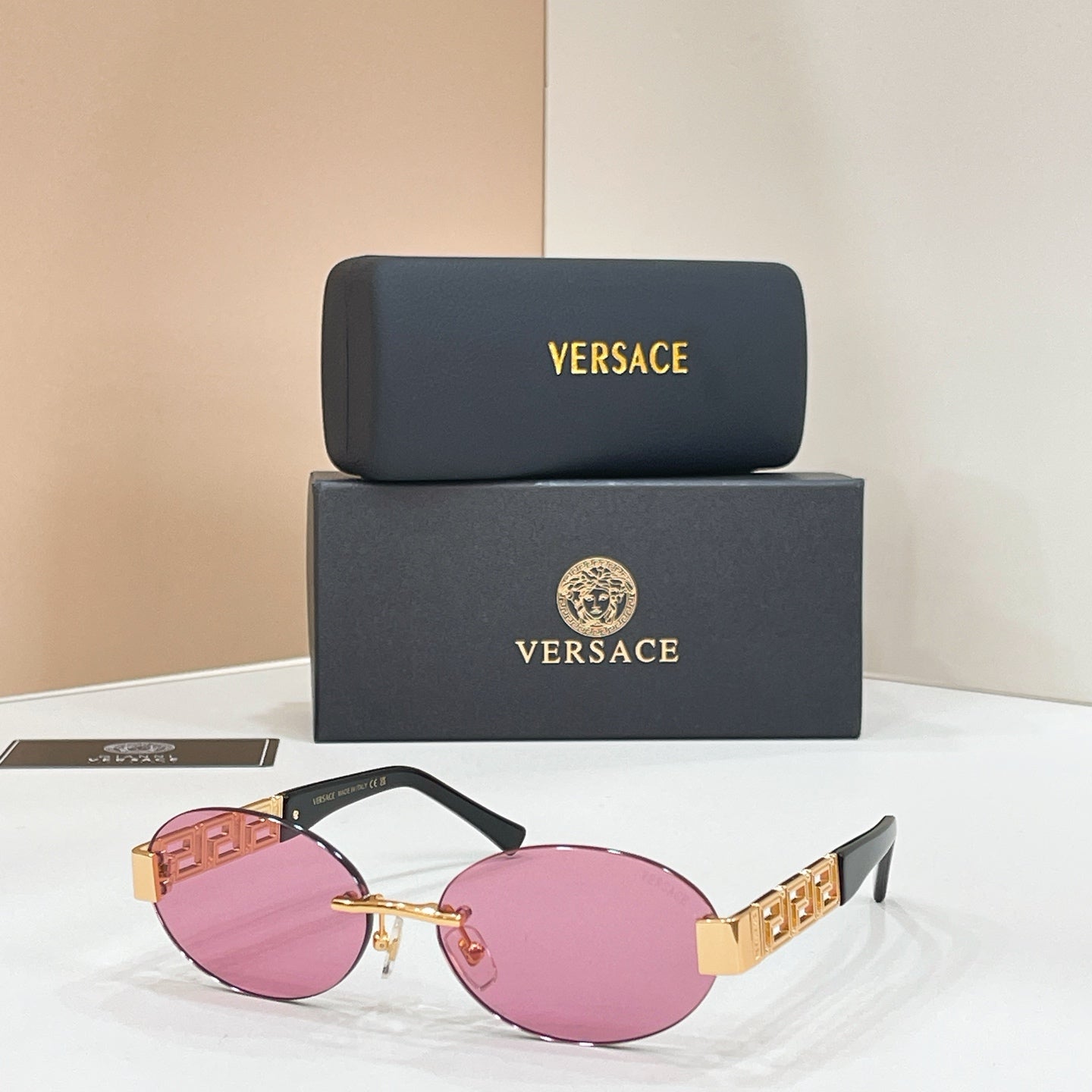 Designer sunglasses with pink tinted lenses, black frame, and gold geometric temples