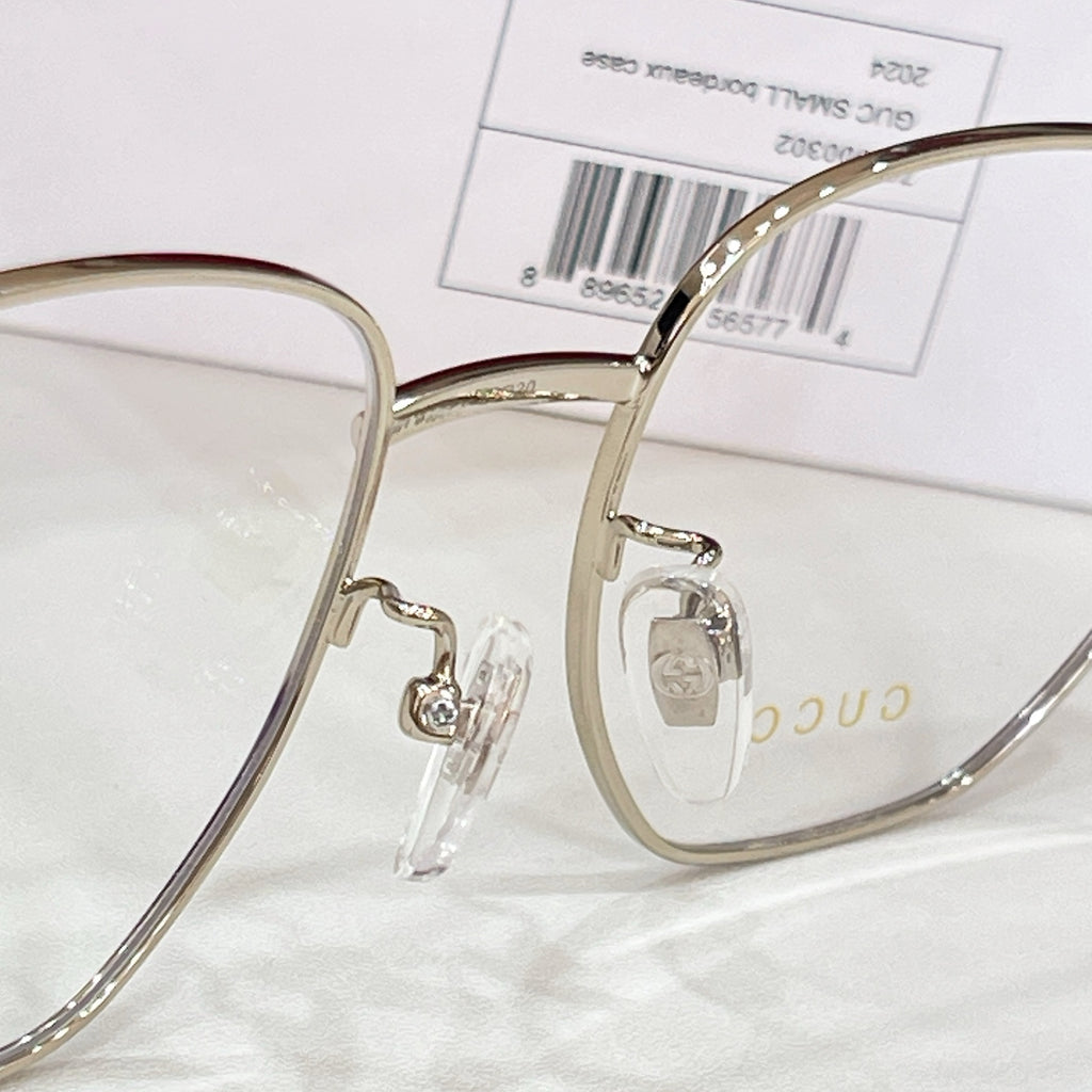 Gold-tone eyeglasses with clear lenses, logo hinge detail, and black temple arm