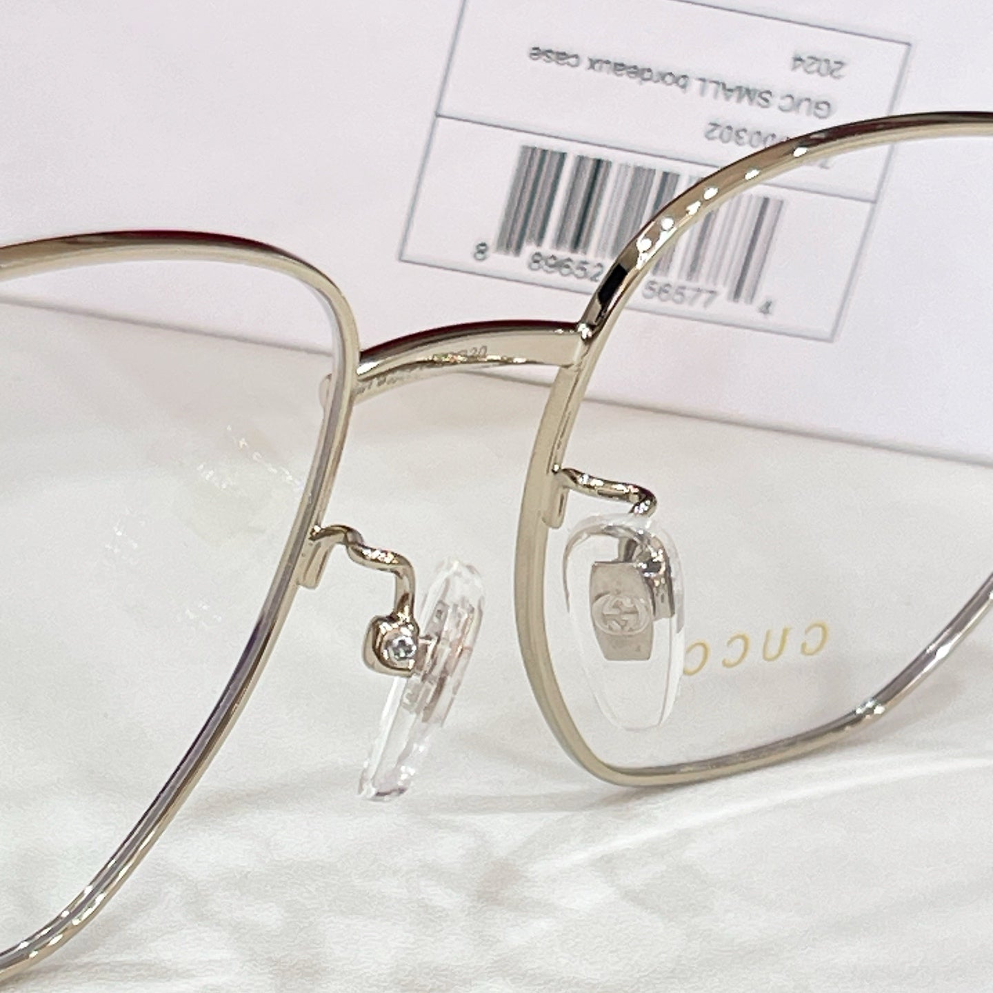 Gold-tone eyeglasses with clear lenses, logo hinge detail, and black temple arm