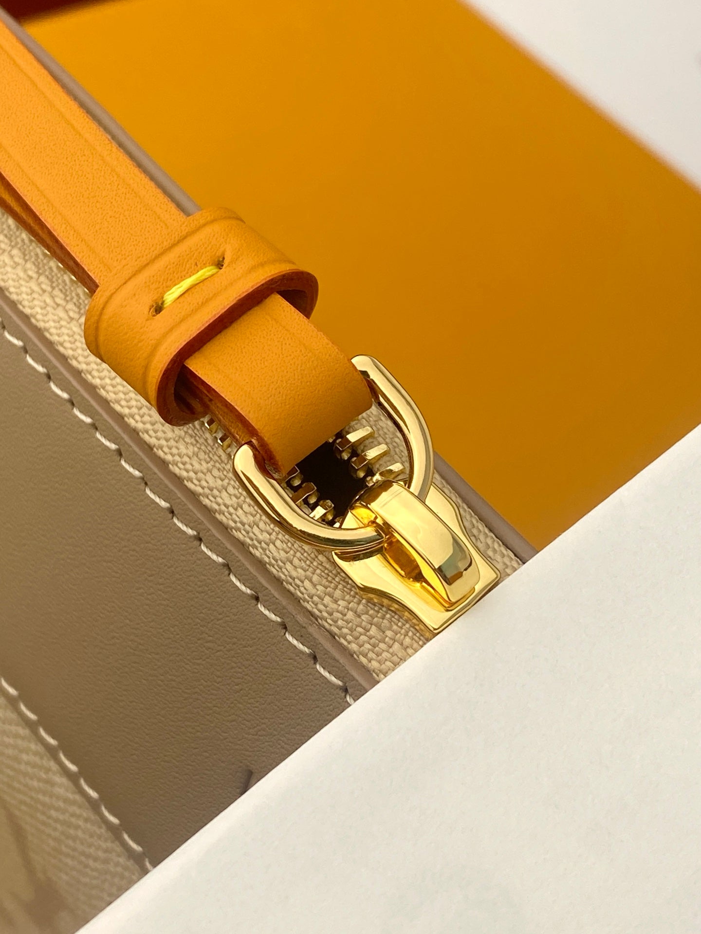 Small leather bag strap end with gold clasp, orange tab and stitched beige edge