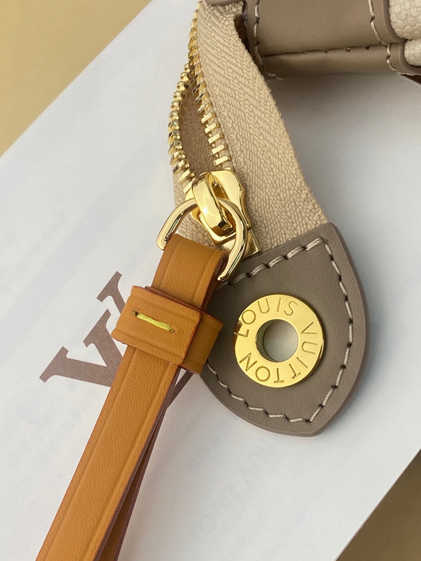 Small pouch bag zipper pull detail, tan leather tab with gold Louis Vuitton disc
