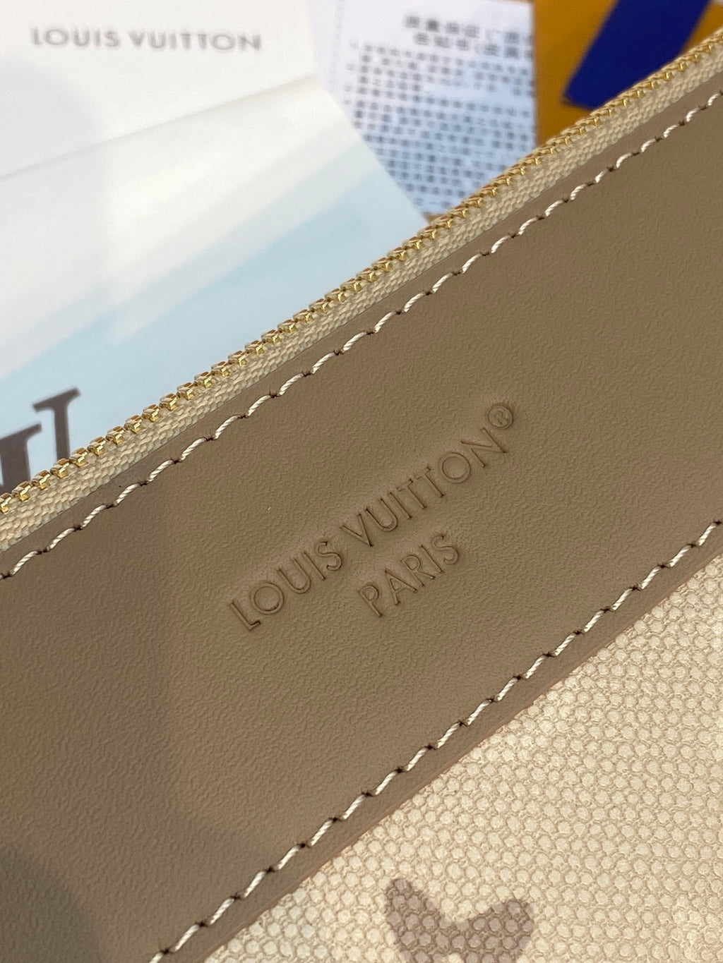Close-up of monogram bag corner with embossed Louis Vuitton-style text and stitched edge