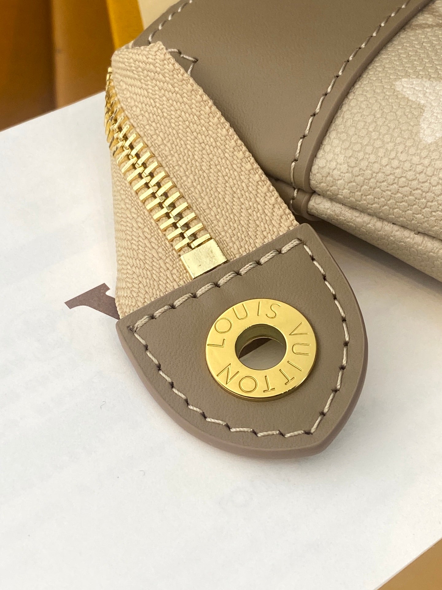 Gold zipper case with monogram bag key charm and tan leather strap, round logo tag