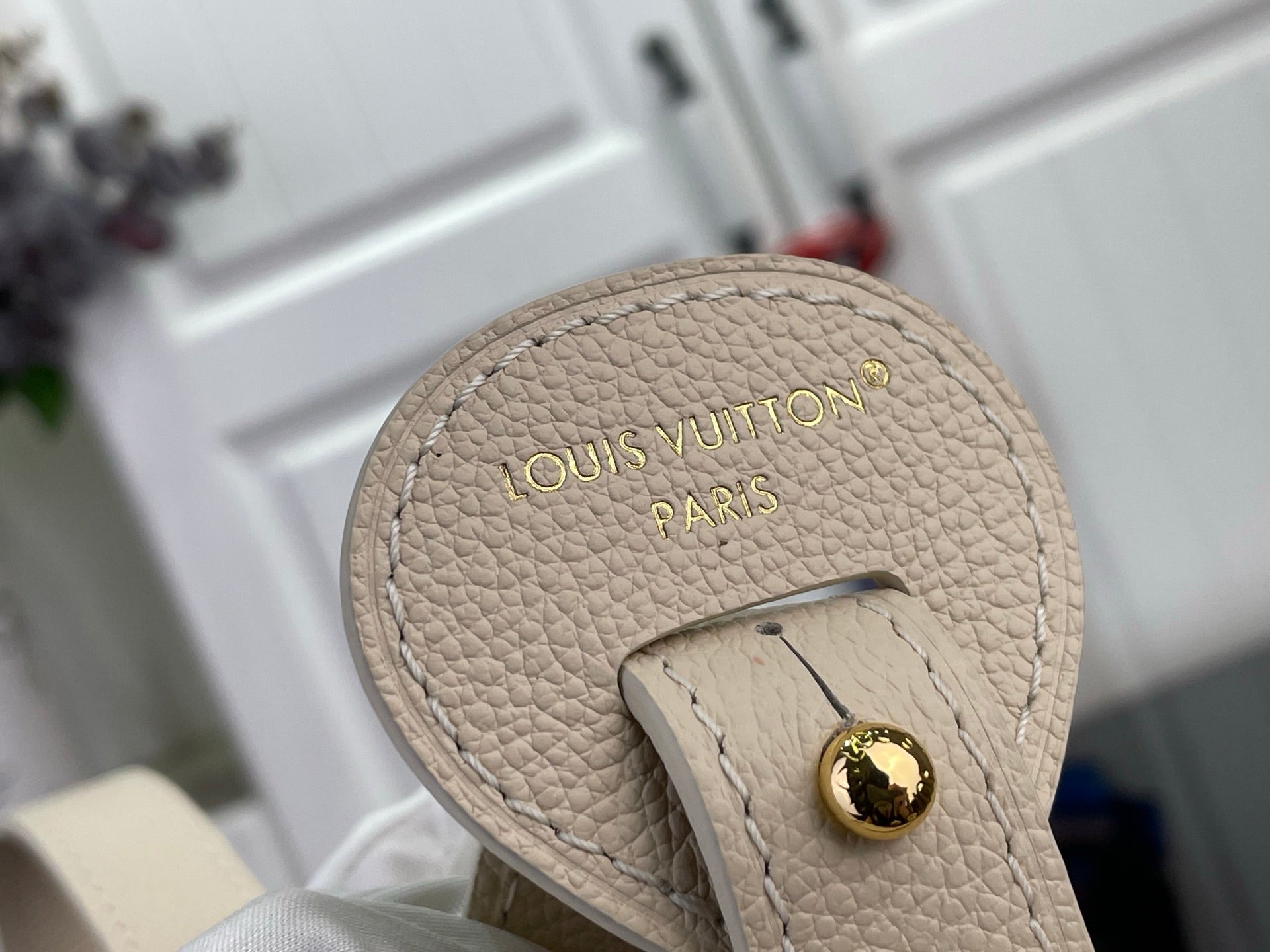 Louis Vuitton bag base with embossed "Louis Vuitton" and gold button on light beige leather