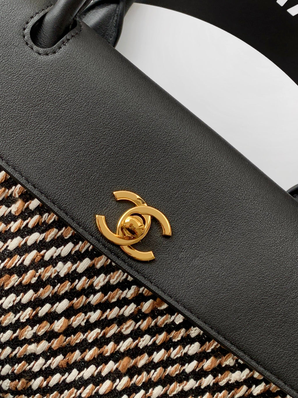 Chanel bag detail: black leather flap with gold CC-style clasp on textured houndstooth.