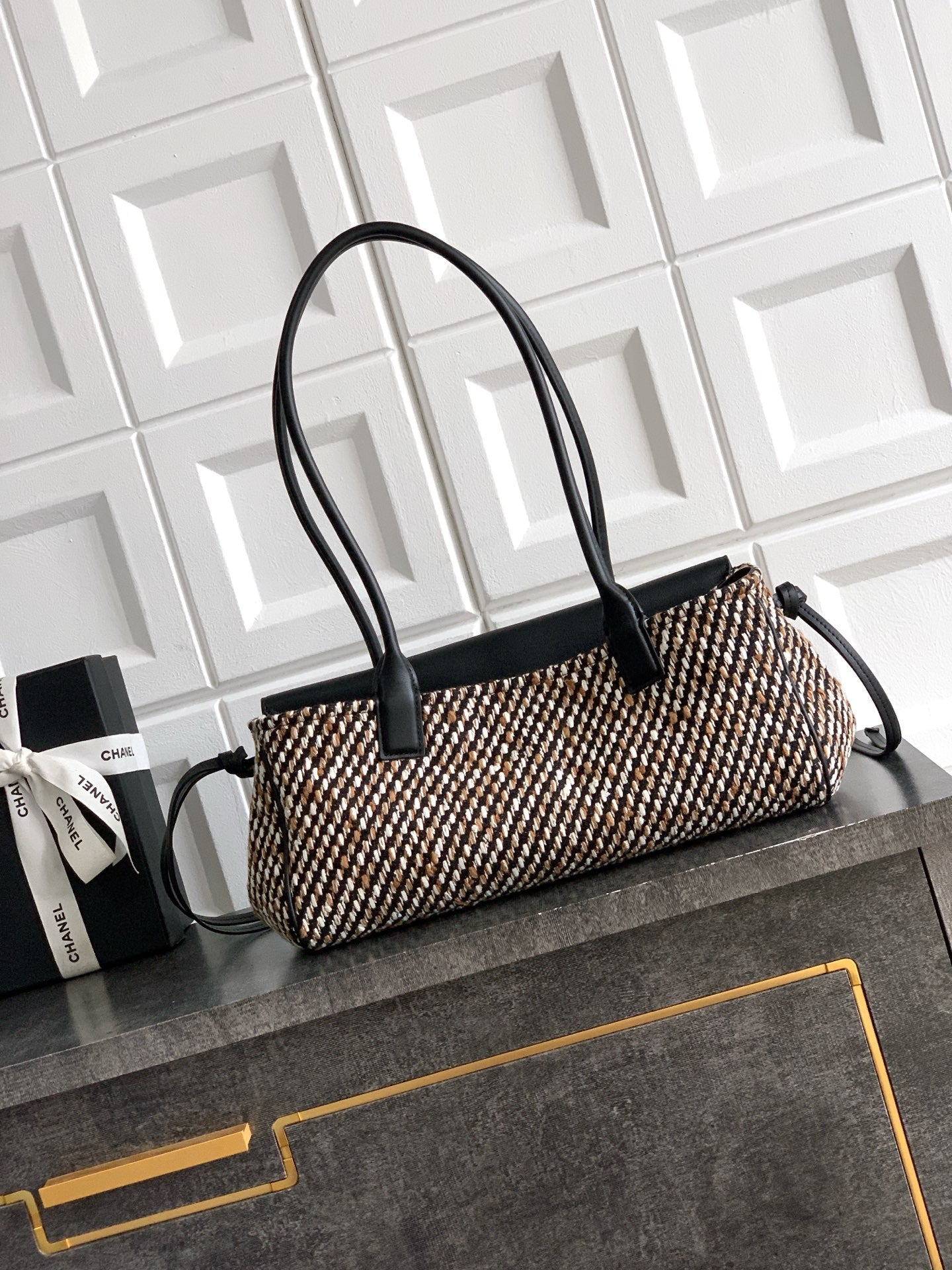 Chanel handbag with black leather handles and rectangular houndstooth woven body, gold logo.