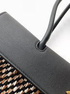 Chanel bag close-up: black leather handle with stitched edge over woven houndstooth.