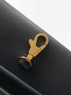 Chanel bag close-up: gold clasp hardware on black leather with stitched seam detail.