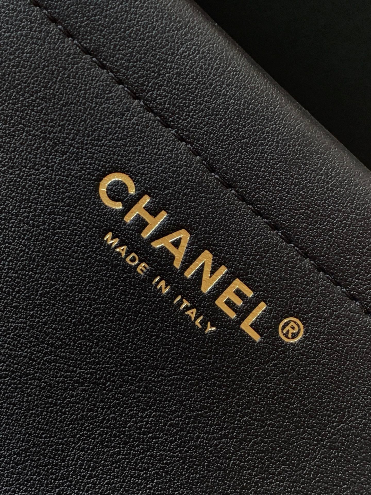 Chanel bag label detail: gold CHANEL text on black leather with stitching.