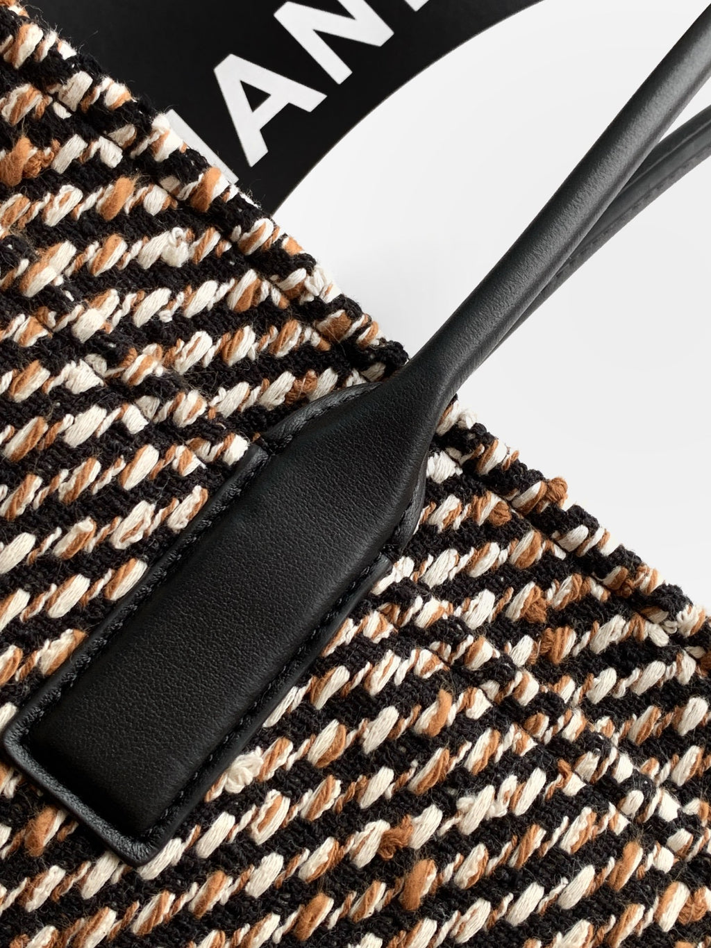 Black leather trim on multicolor tweed handbag with visible stitching and edge panel