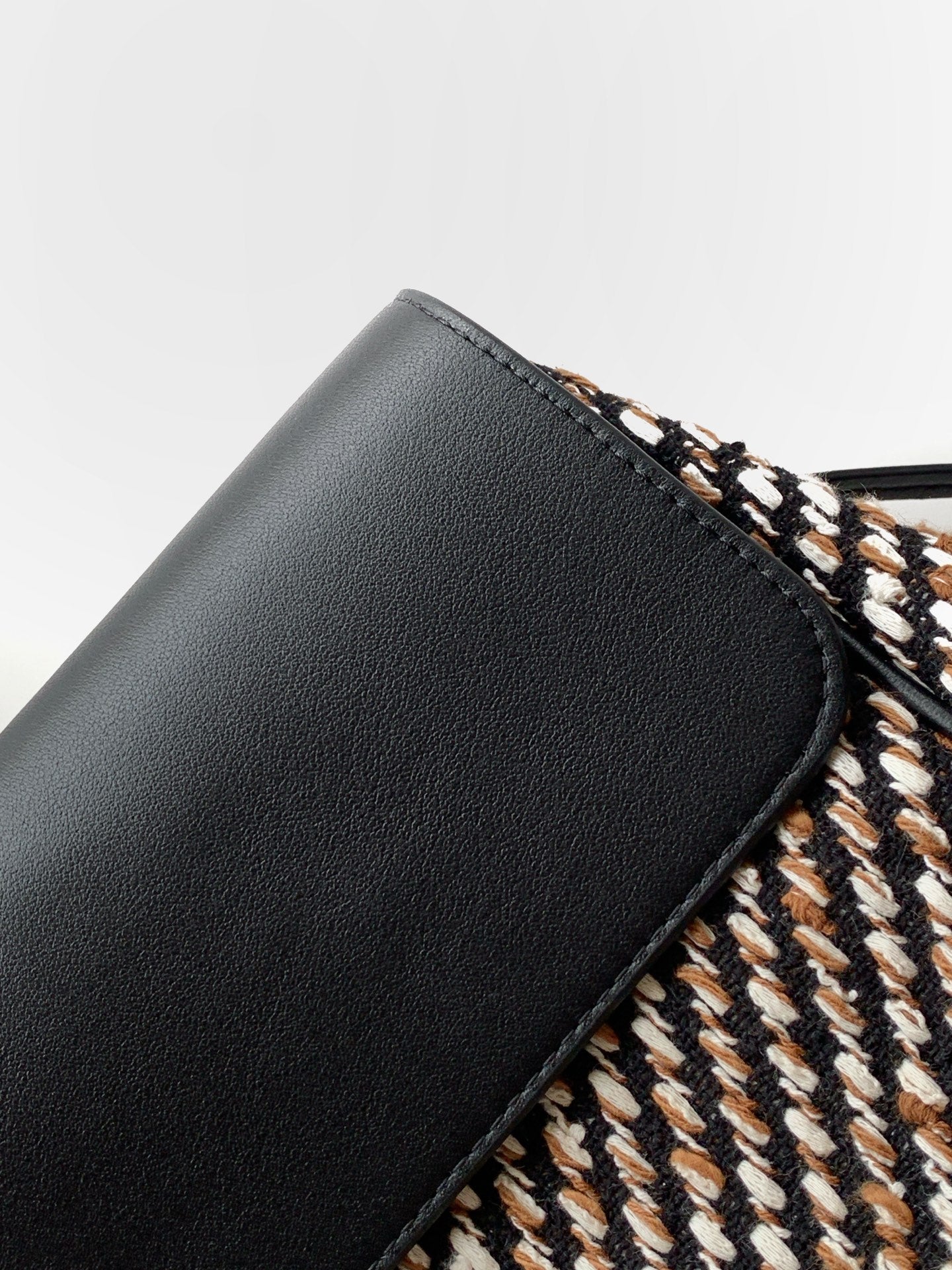 Black leather corner of tweed handbag with trim edge and stitched seam detail
