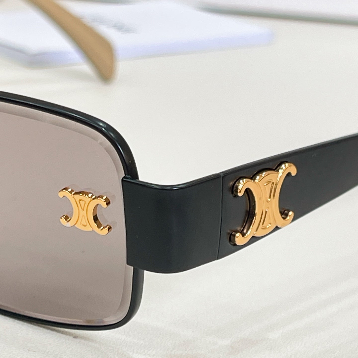 Close-up: black sunglasses temple with gold logo detail and clear lenses