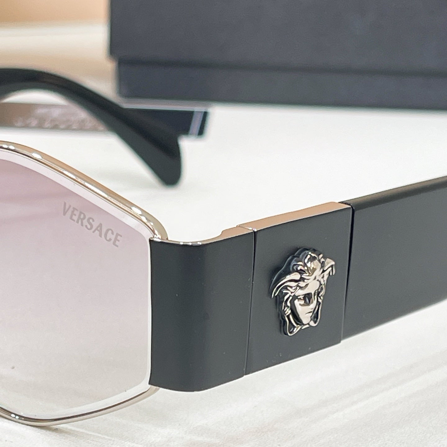 Versace sunglasses side detail, black temple with gold lion emblem and dark lens