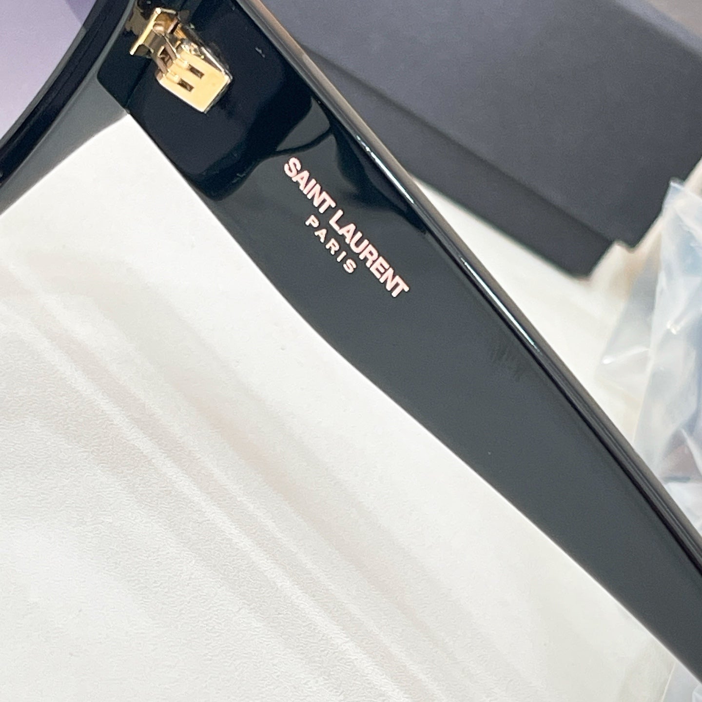 Black sunglasses arm with 'SAINT LAURENT PARIS' text and gold hinge detail.