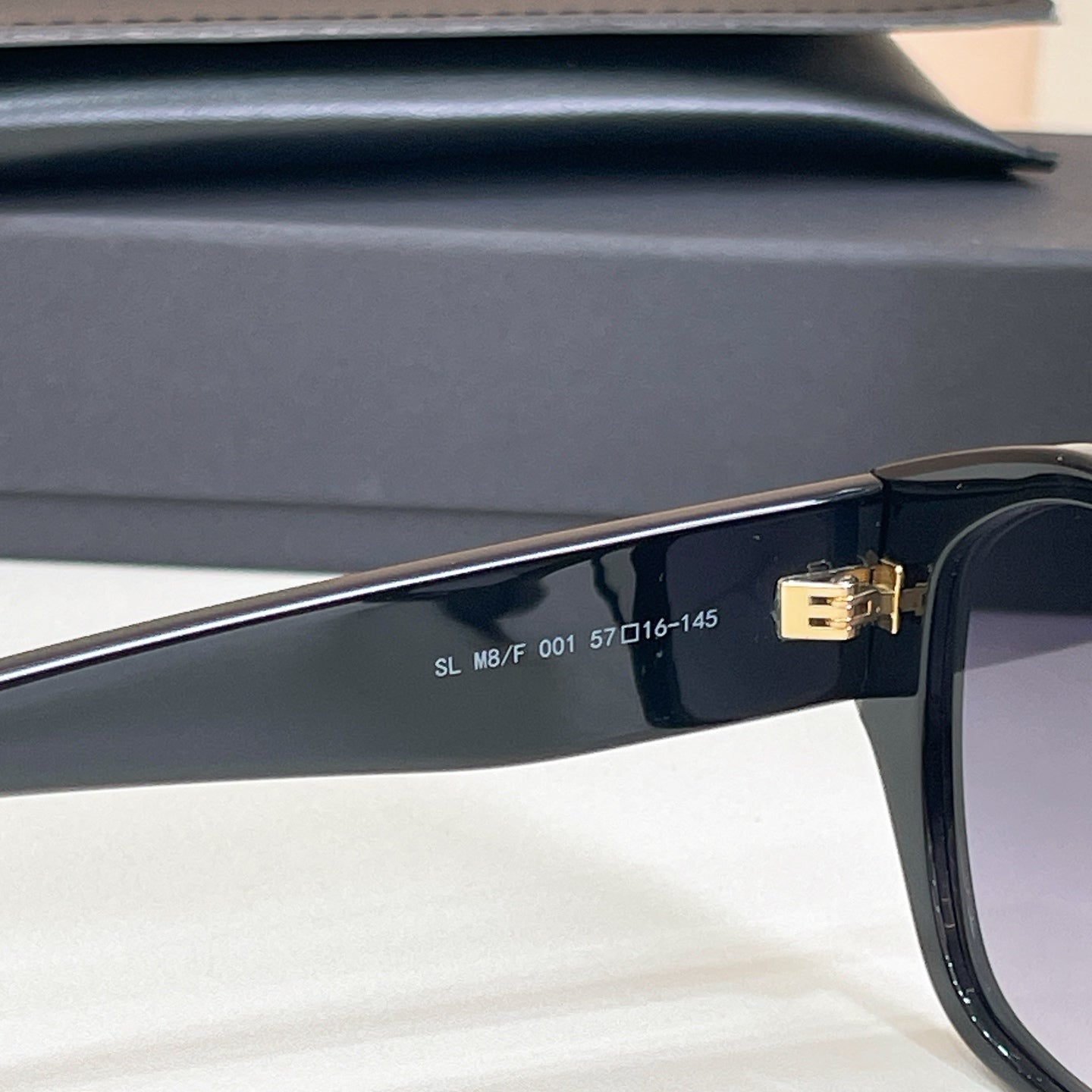 Black sunglasses temple close-up with engraved markings and gold hinge detail.