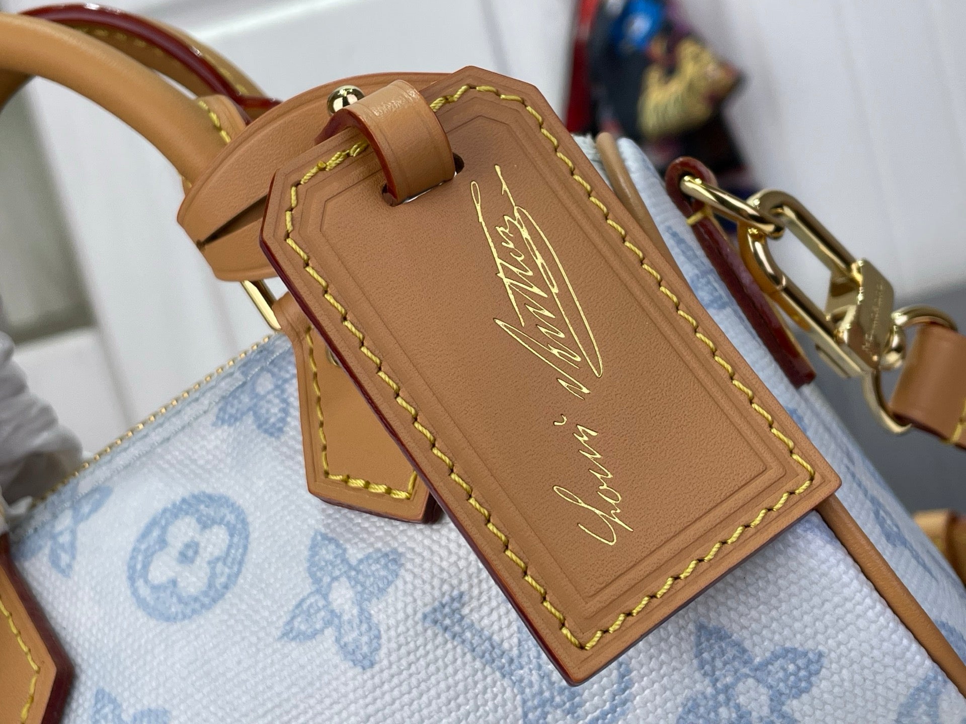 Louis Vuitton tan leather tag with gold stitching on light blue monogram bag