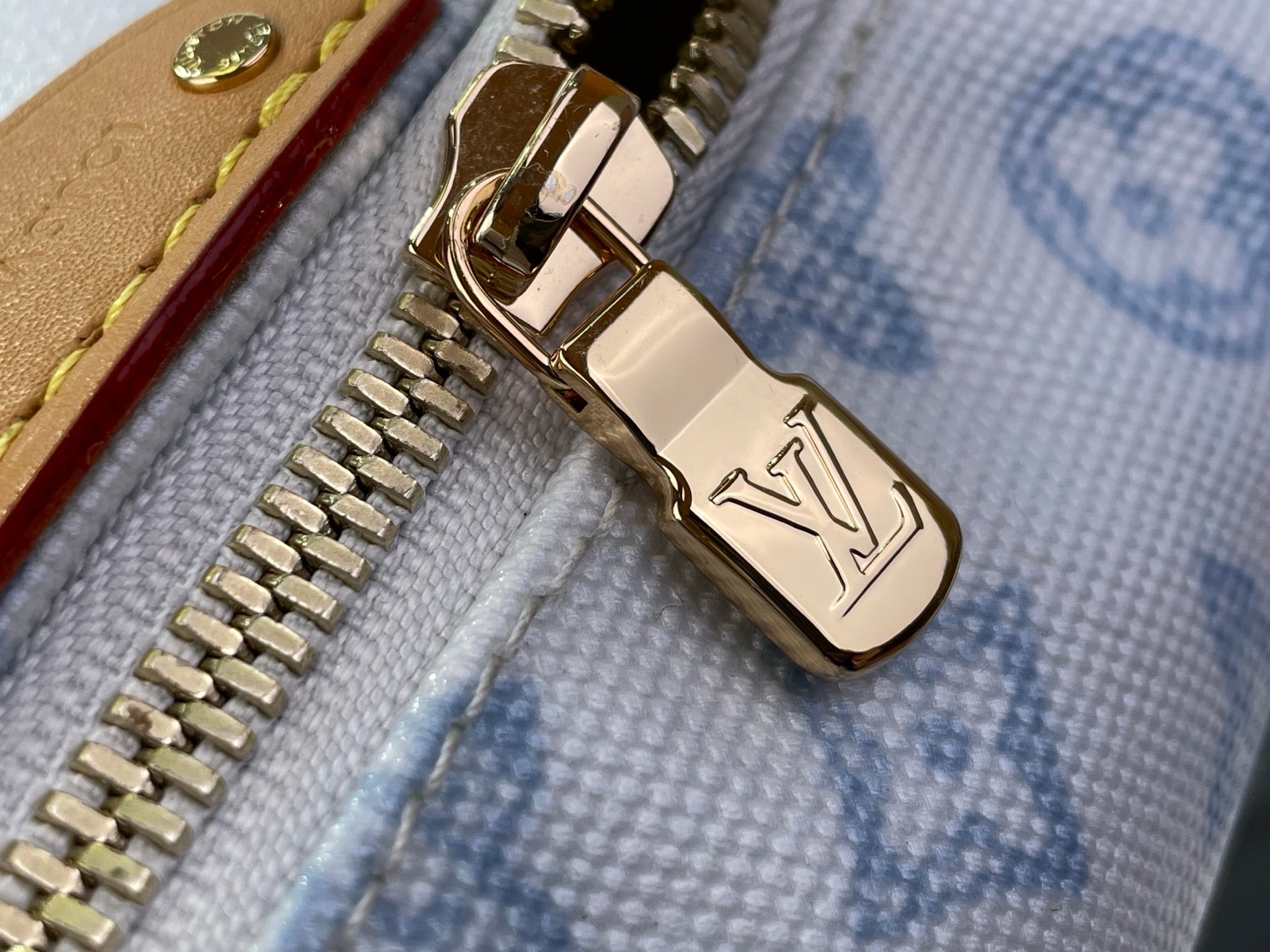 Gold metal zipper pull on light blue monogram canvas bag with zipper teeth
