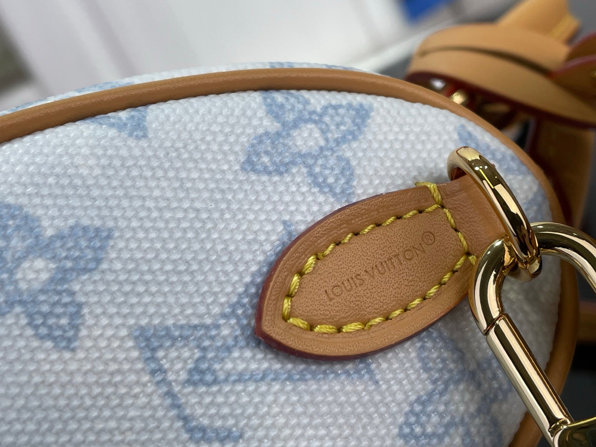 Tan leather loop patch with gold stitching and Louis Vuitton monogram on blue fabric.