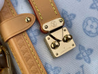 Blue monogram handbag close-up: tan leather strap with gold buckles and logo plates