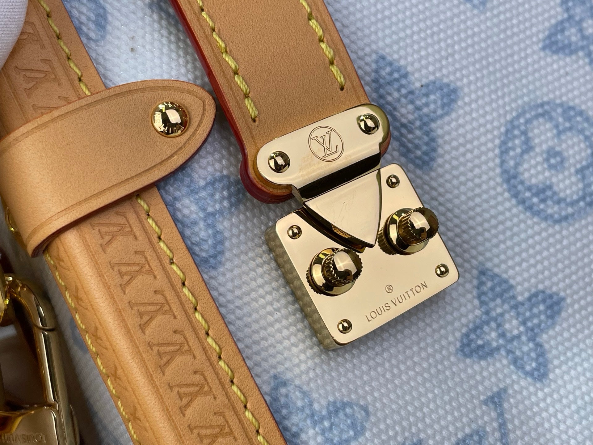 Blue monogram handbag close-up: tan leather strap with gold buckles and logo plates