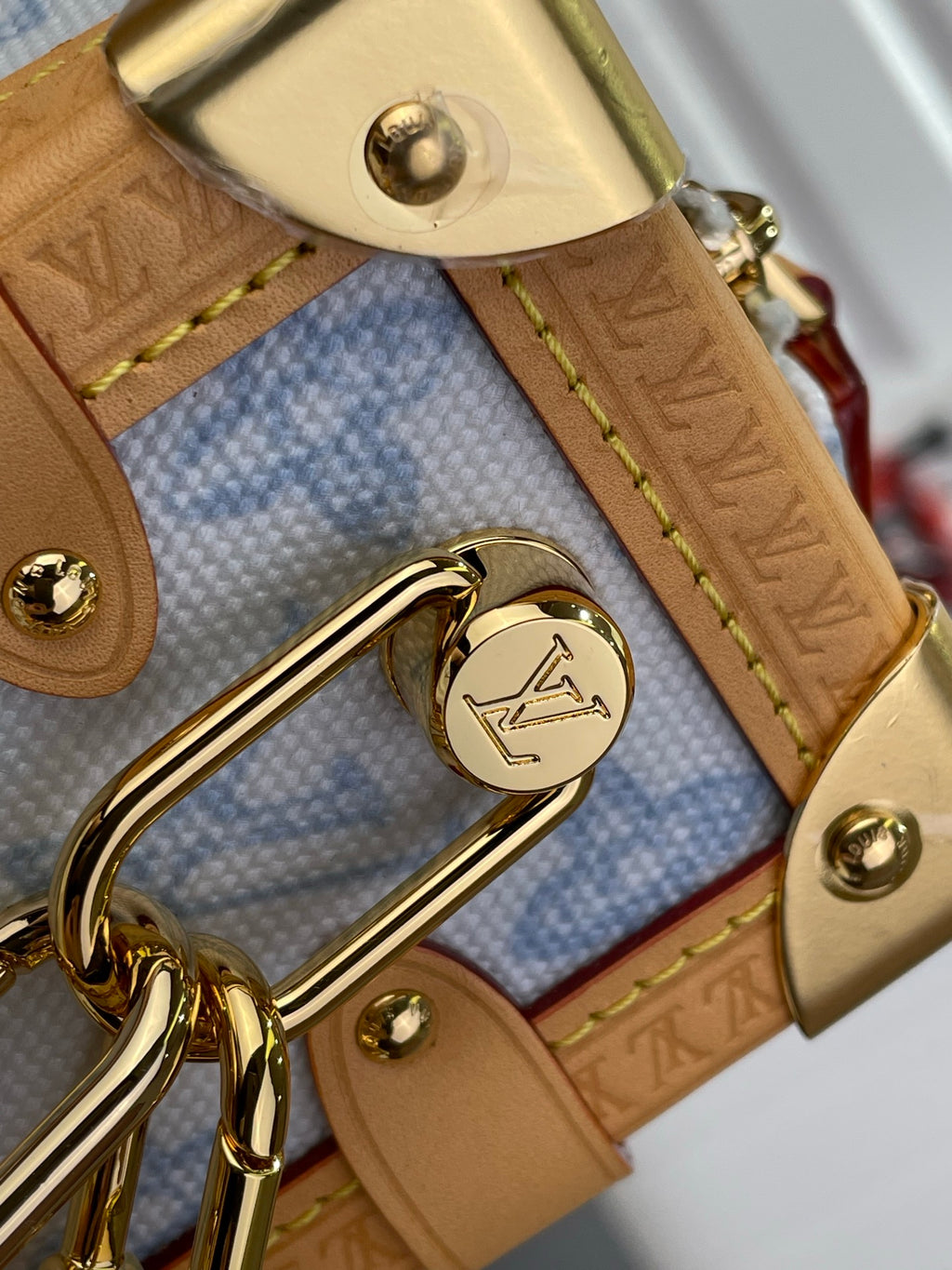 Blue monogram handbag close-up: gold logo ring on tan leather strap