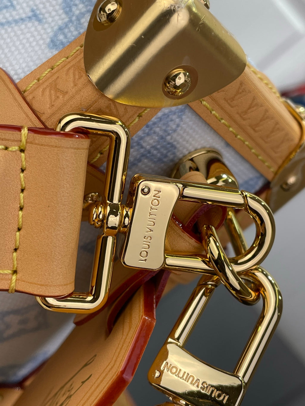 Blue monogram handbag close-up: gold clasp and key ring hardware with tan leather