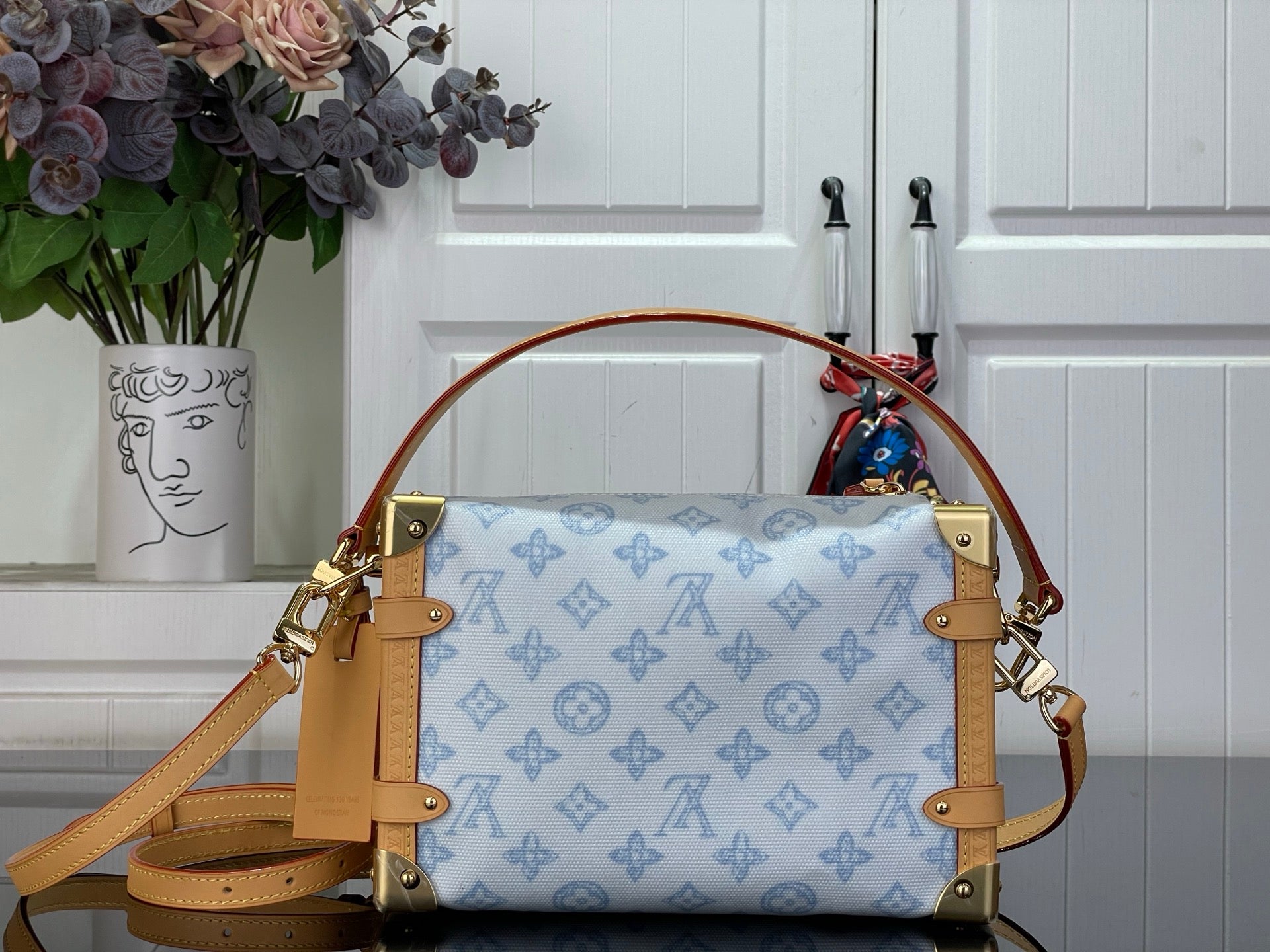 Blue monogram handbag with tan leather handles, gold hardware, and crossbody strap