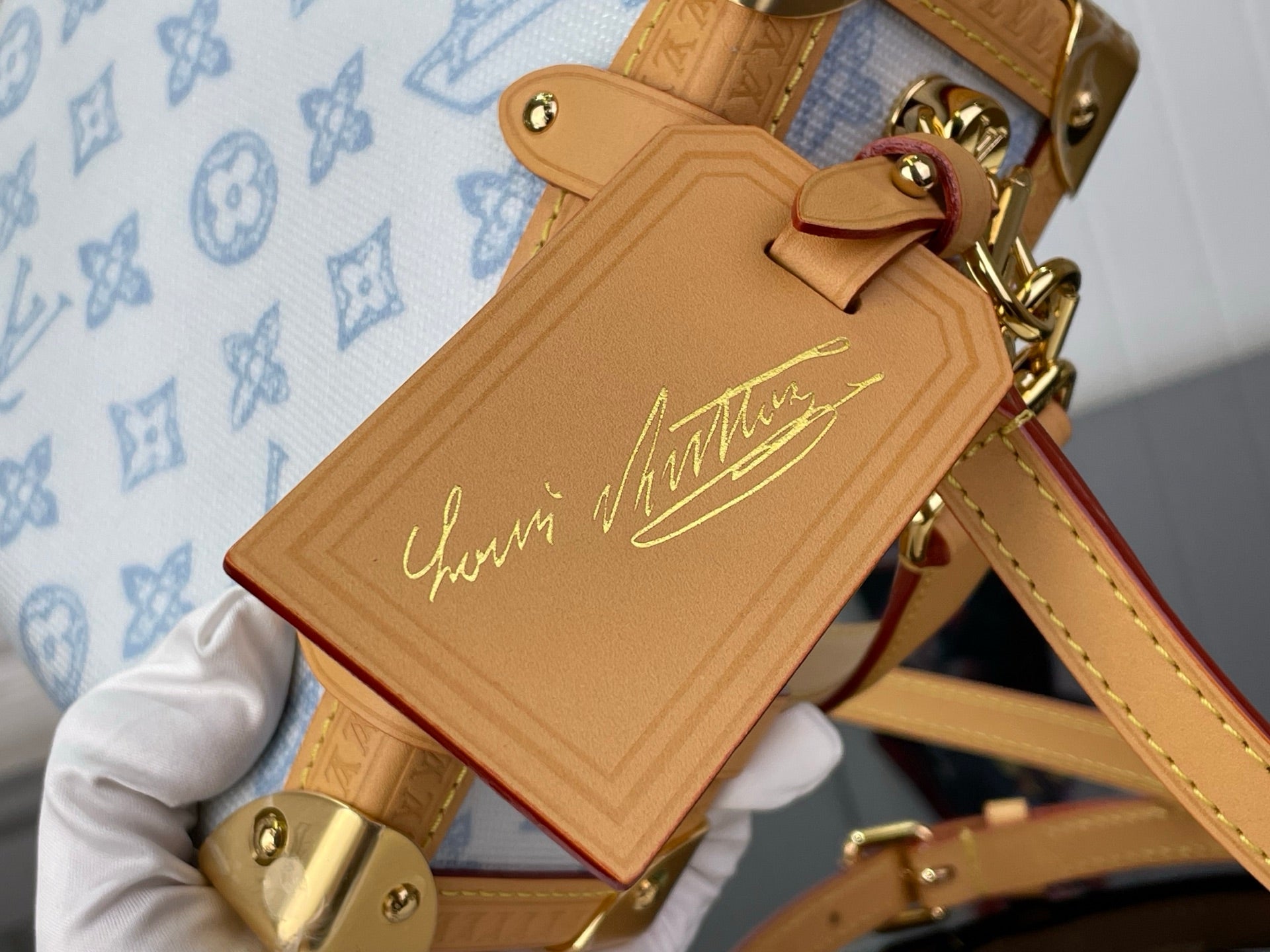 Blue monogram handbag close-up: tan leather signature tag with gold hardware