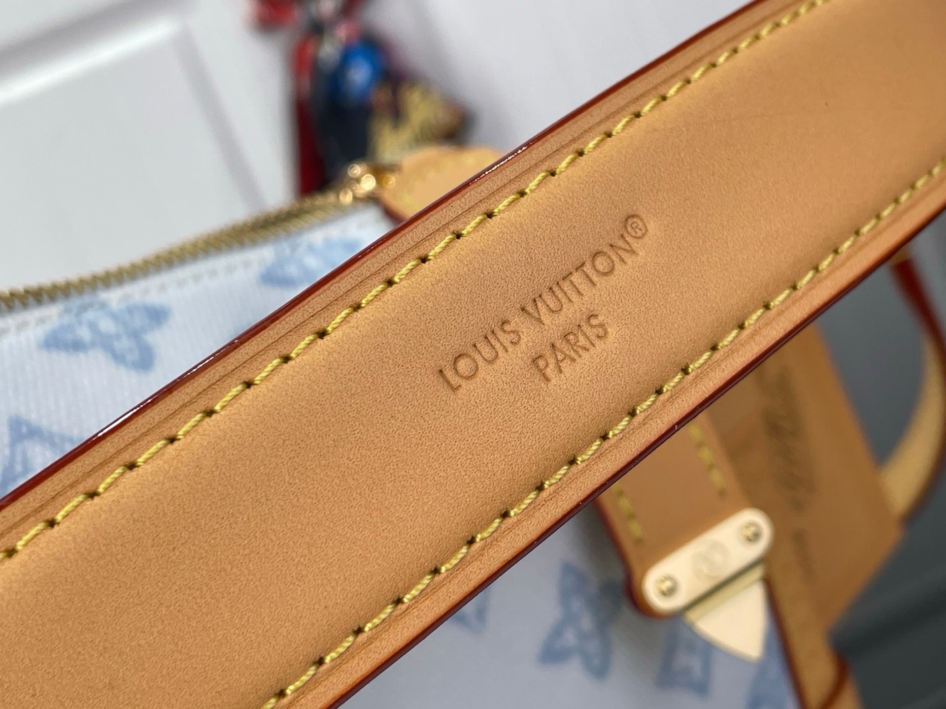 Tan leather bag strap edge with stamped 'LOUIS VUITTON PARIS' text and yellow stitching