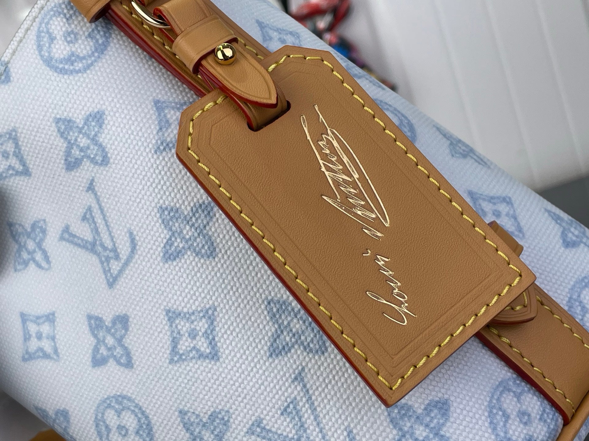 Louis Vuitton bag strap detail on light blue monogram canvas with tan leather patch and stitching
