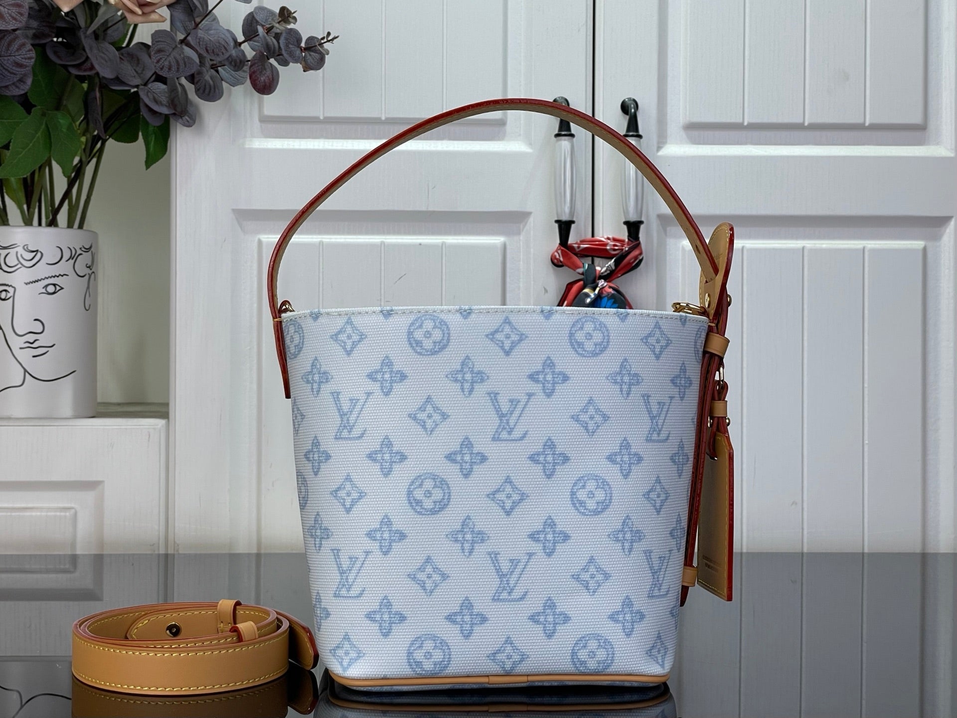 Louis Vuitton tote bag with light blue monogram print, tan straps, and leather side tabs