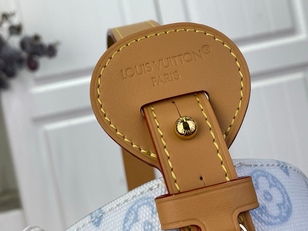 Louis Vuitton bag leather tab with “LOUIS VUITTON PARIS” and gold clasp over light blue canvas