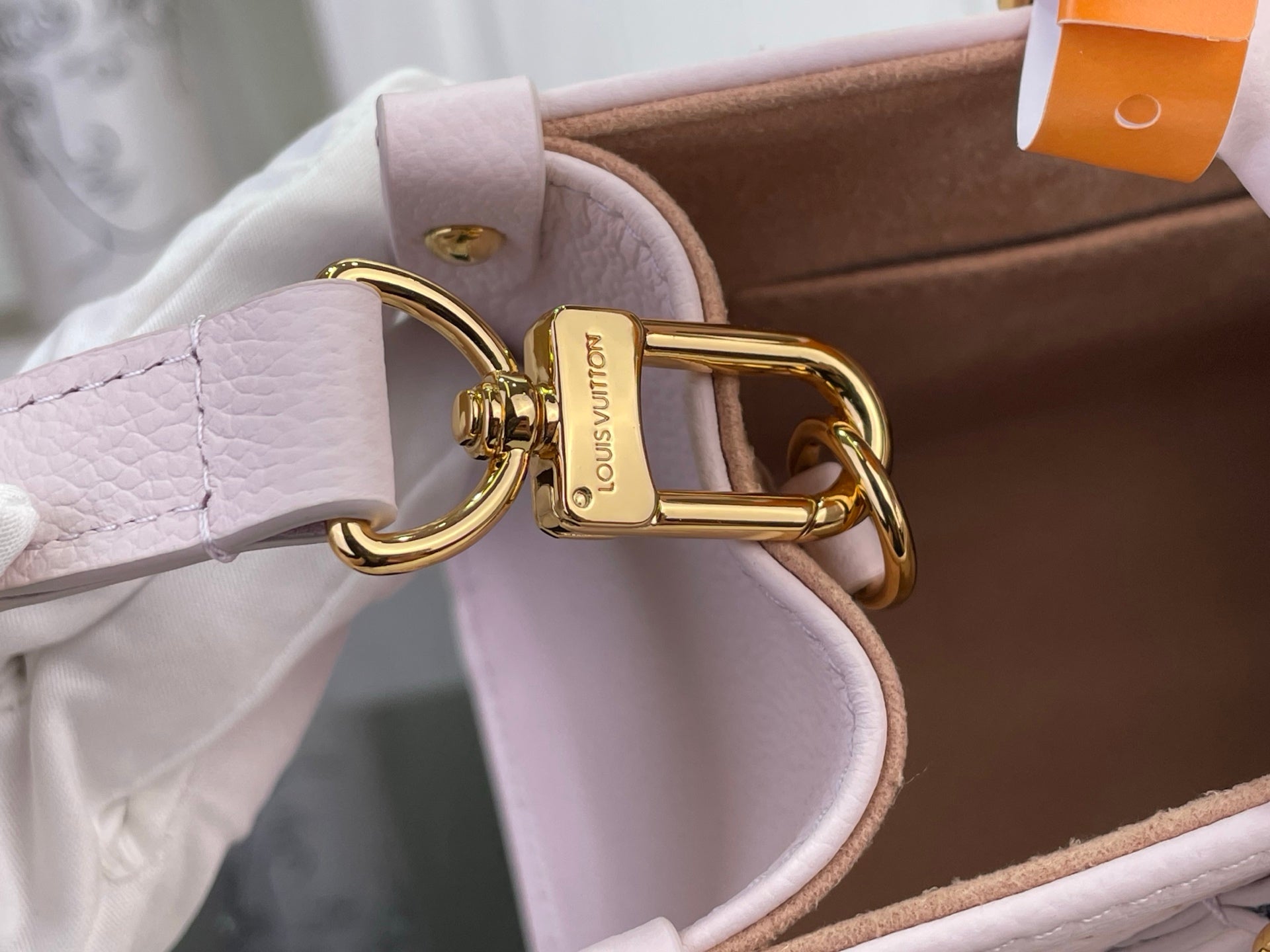 Light pink leather shoulder strap with gold buckle hardware and embossed brand tag