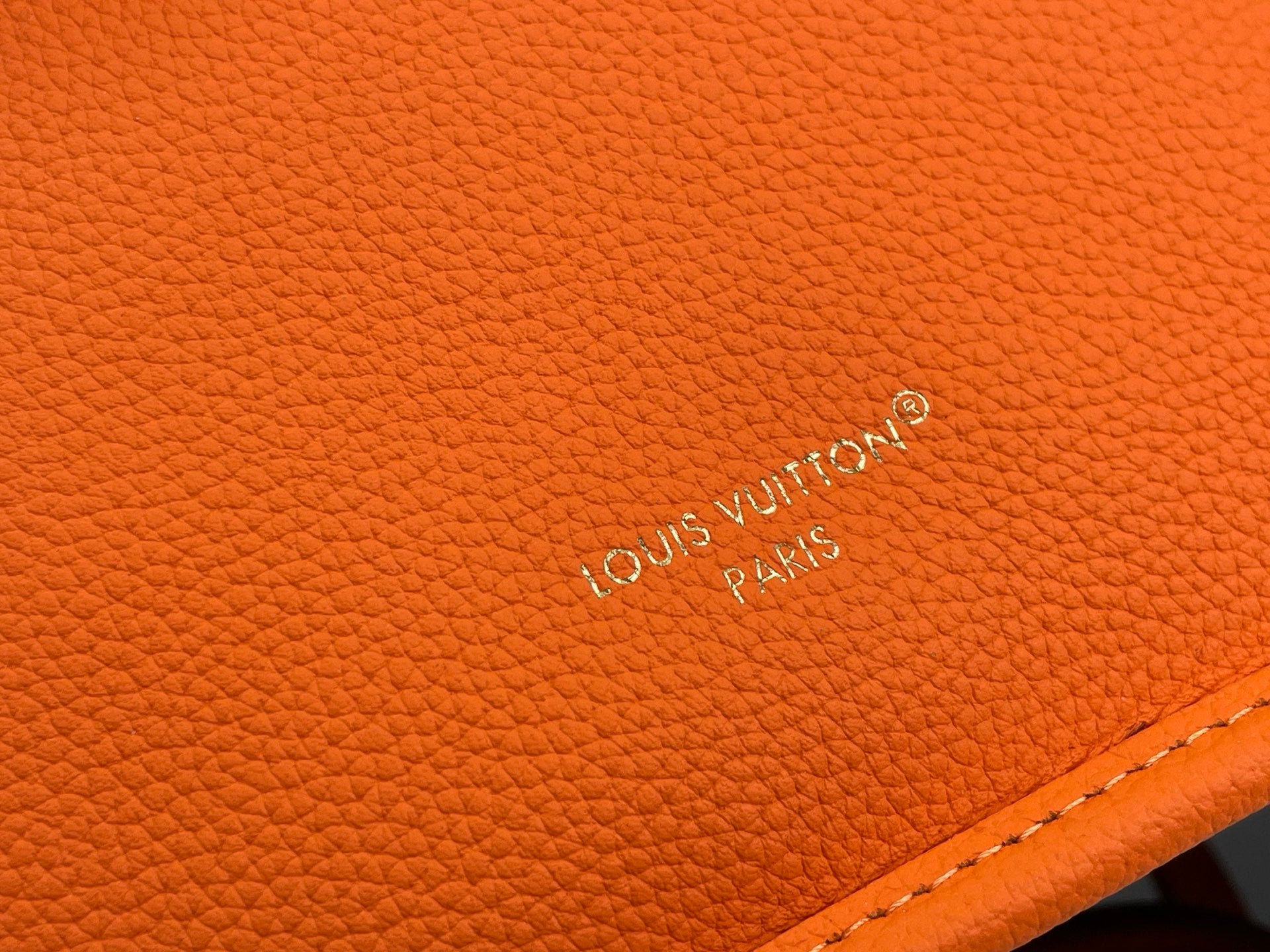 Orange pebbled leather bag with engraved LV logo on the surface