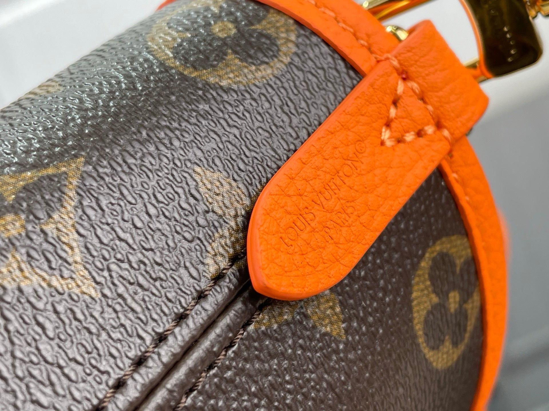 Louis Vuitton monogram bag corner with orange leather strap and close-up stitching