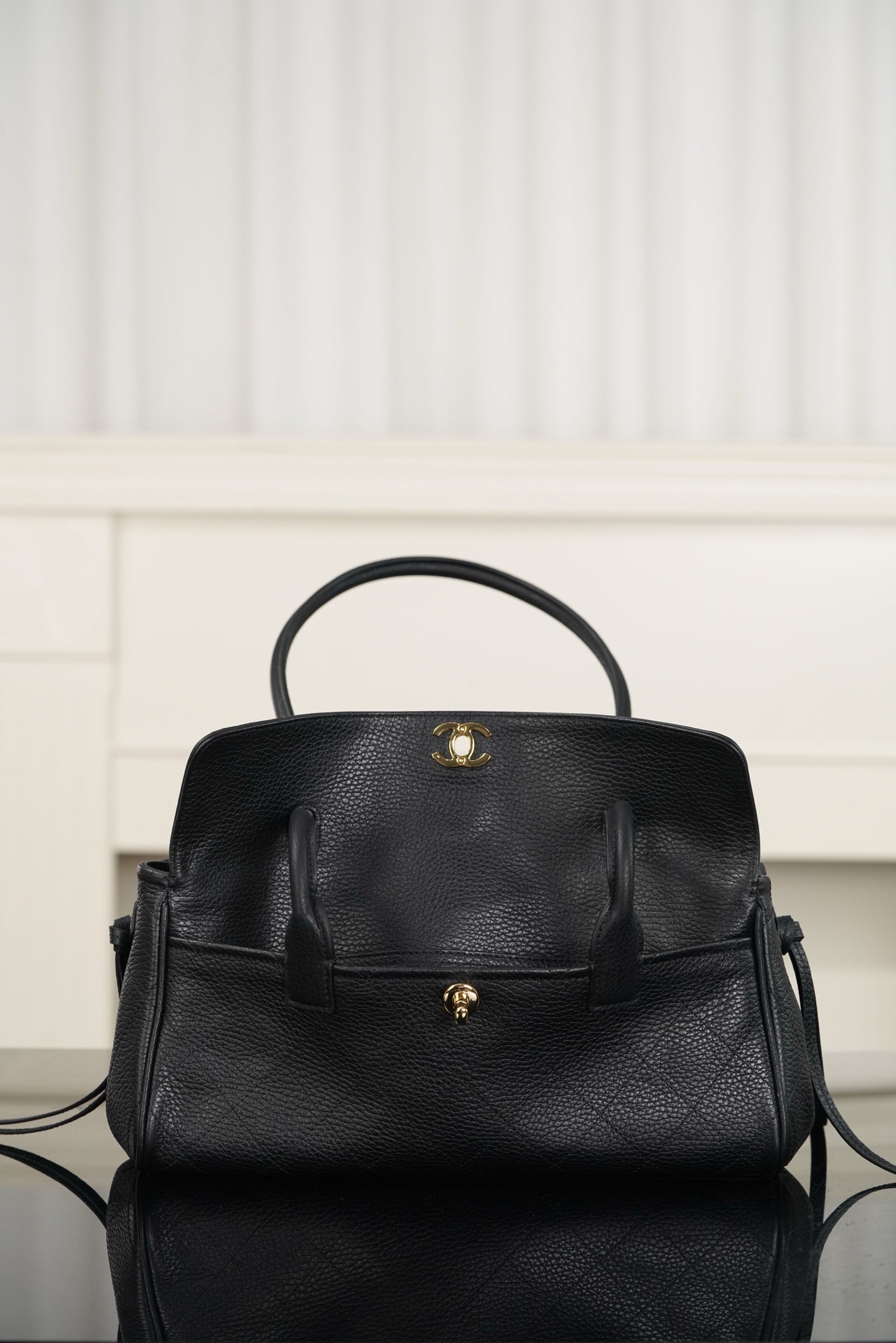Chanel handbag front view in dark leather, flap cover, small gold top clasp, short handles