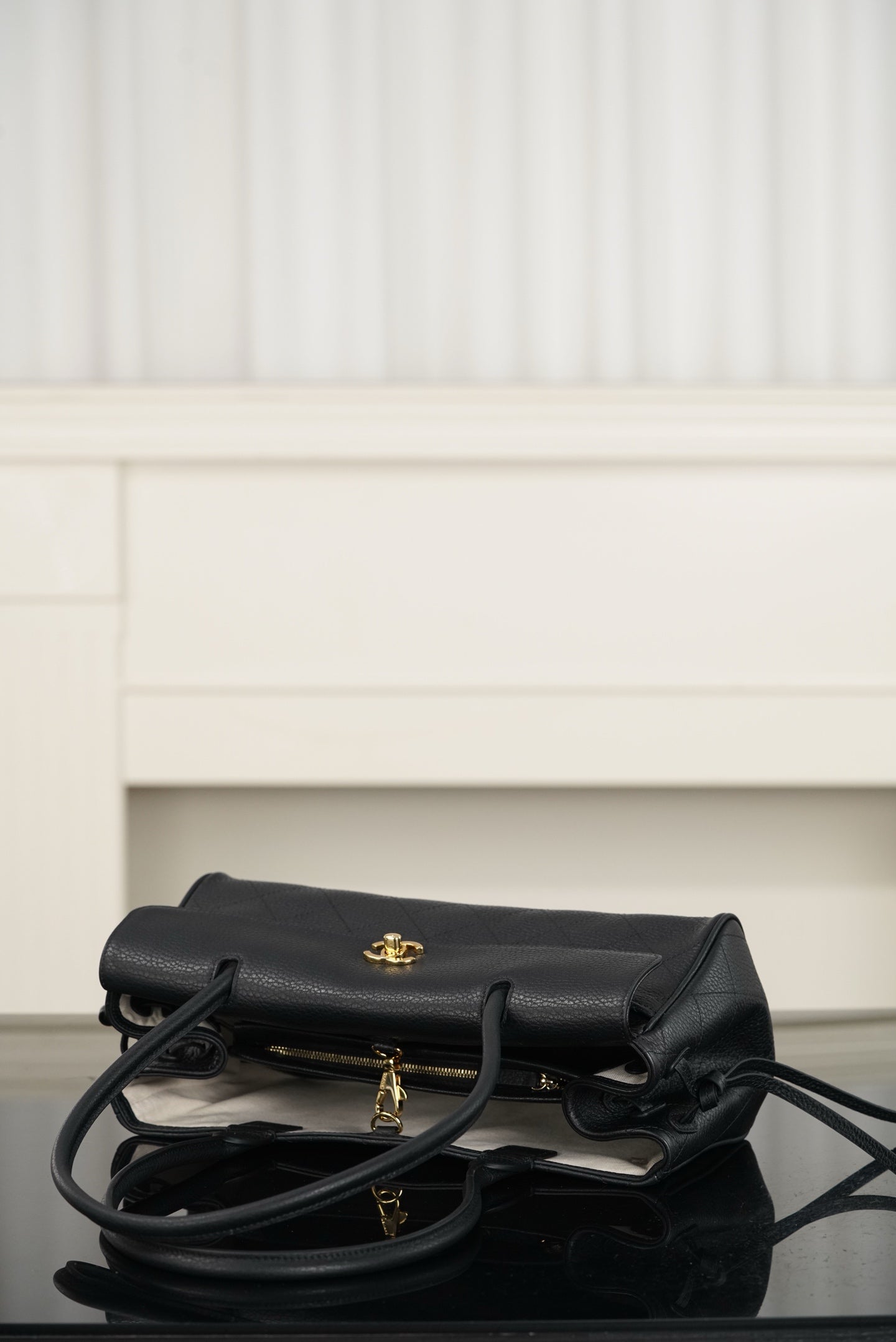 Chanel handbag lying flat in dark leather, flap with gold logo, crossbody strap visible