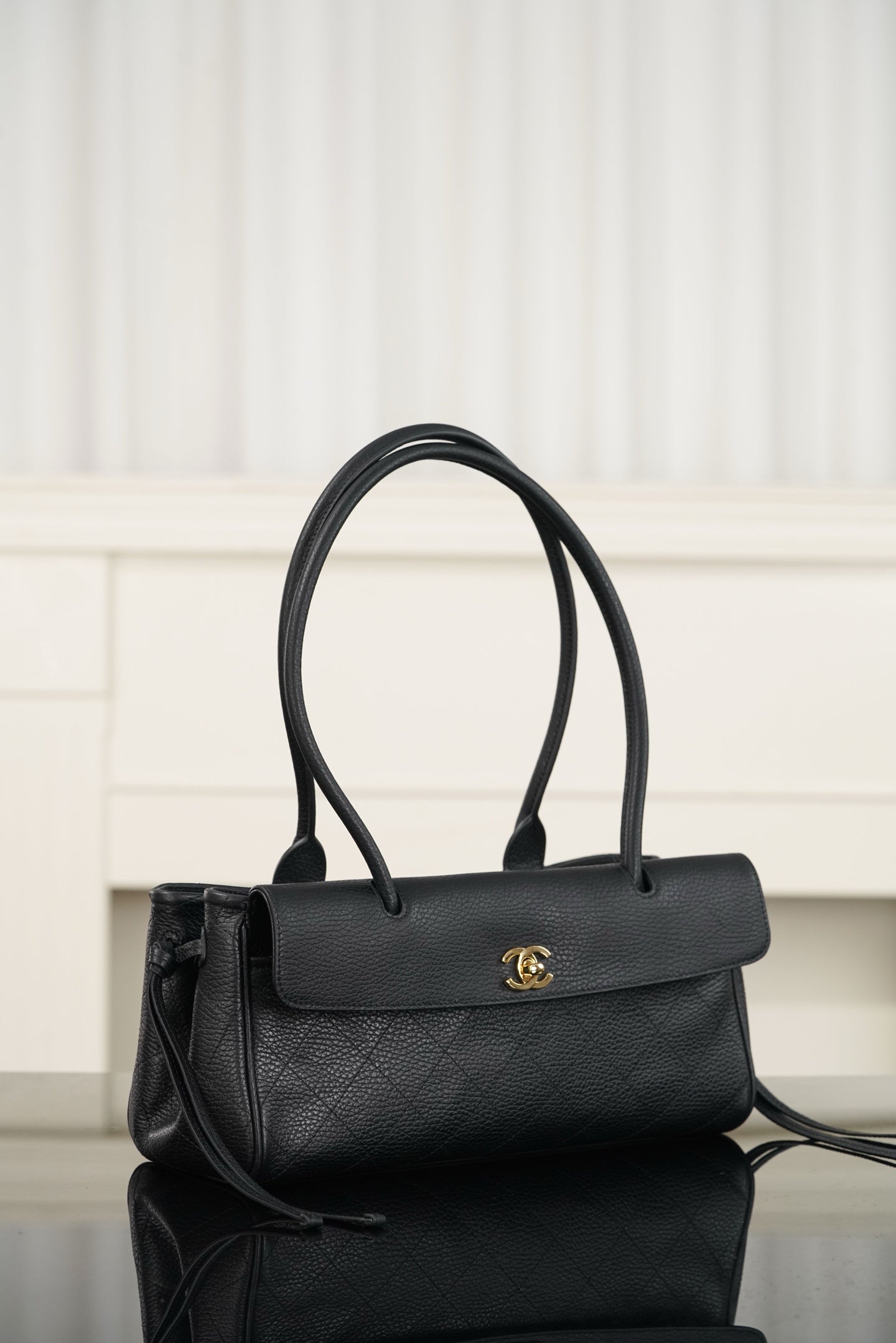 Chanel handbag in dark textured leather, flap with gold logo, side angle with strap