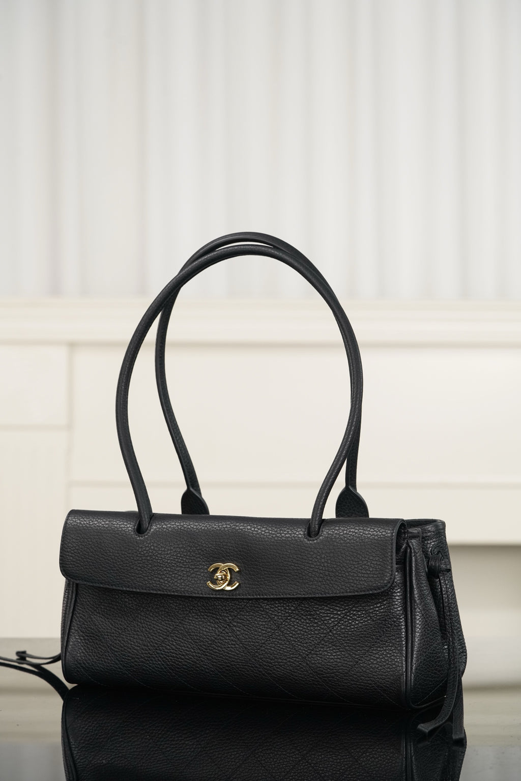 Chanel handbag with dark leather flap, gold logo emblem, top handles and shoulder strap