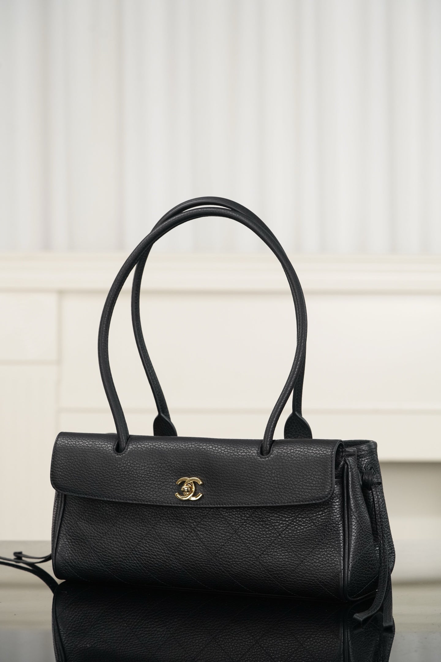 Chanel handbag with dark leather flap, gold logo emblem, top handles and shoulder strap