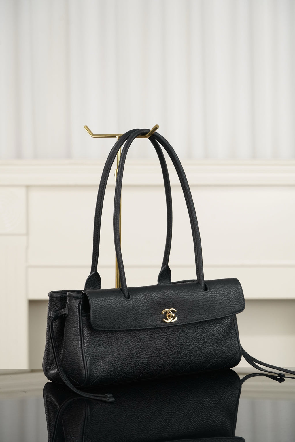Chanel handbag in dark leather with top handle, flap front and gold logo, side view