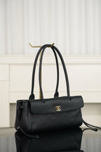 Chanel handbag in dark leather with top handle, flap front and gold logo, side view