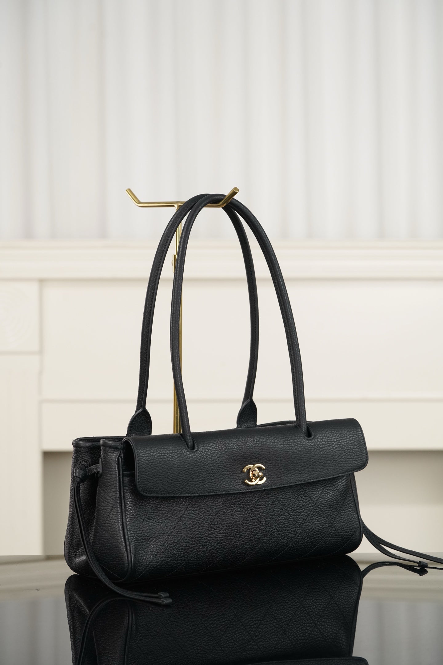 Chanel handbag in dark leather with top handle, flap front and gold logo, side view