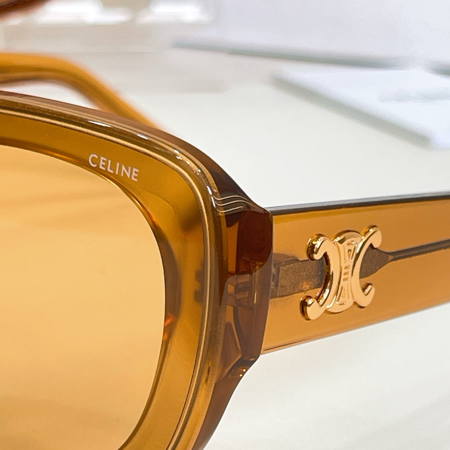 Close-up of amber sunglasses arm with gold-tone logo detail and hinge
