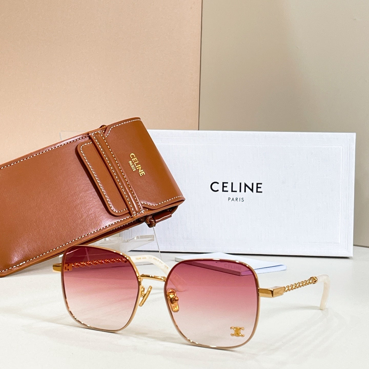 Sunglasses with round pink gradient lenses, gold-tone frame, and chain-link temple arms
